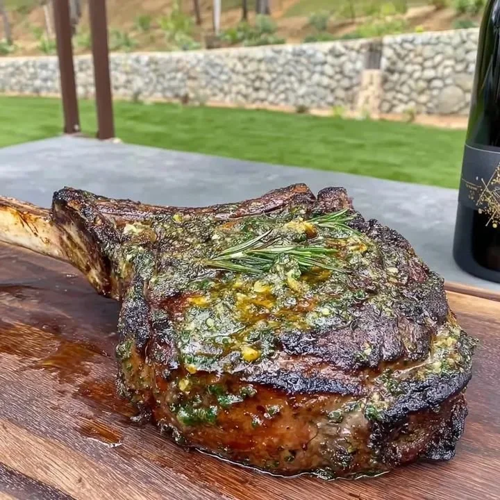 Saftiges Tomahawk Steak mit Kräuterbutter auf dem Grill serviert.